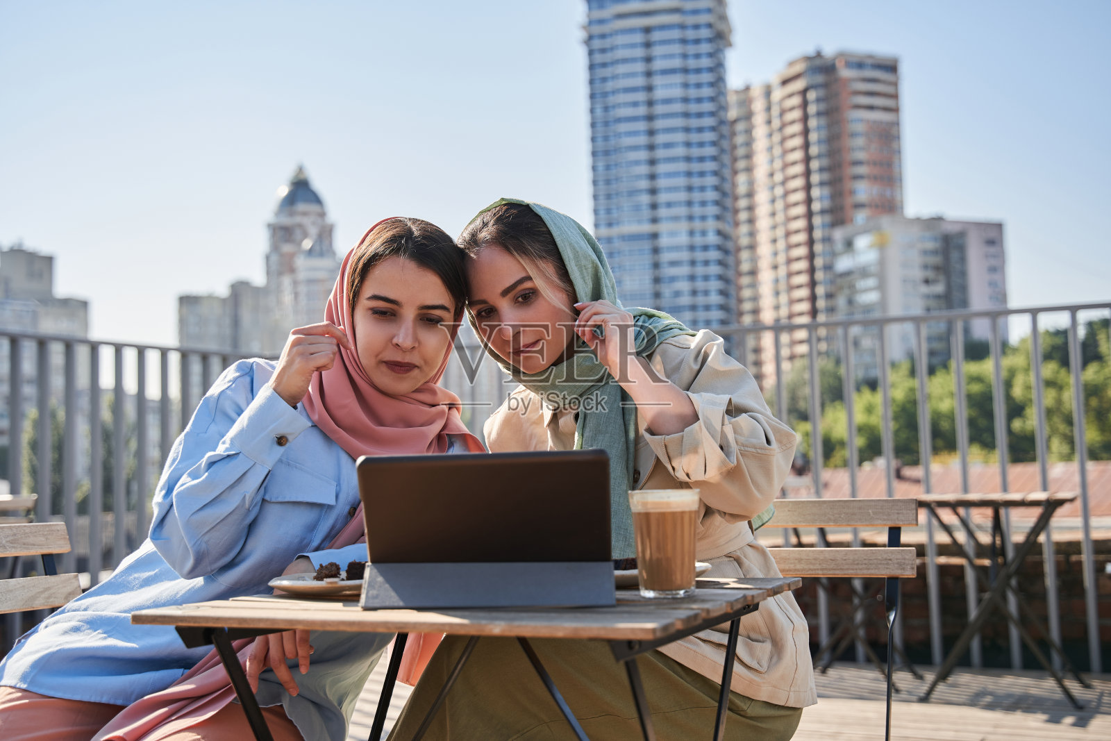阿拉伯妇女穿着长袍坐在自助餐厅喝着咖啡，看着平板电脑照片摄影图片
