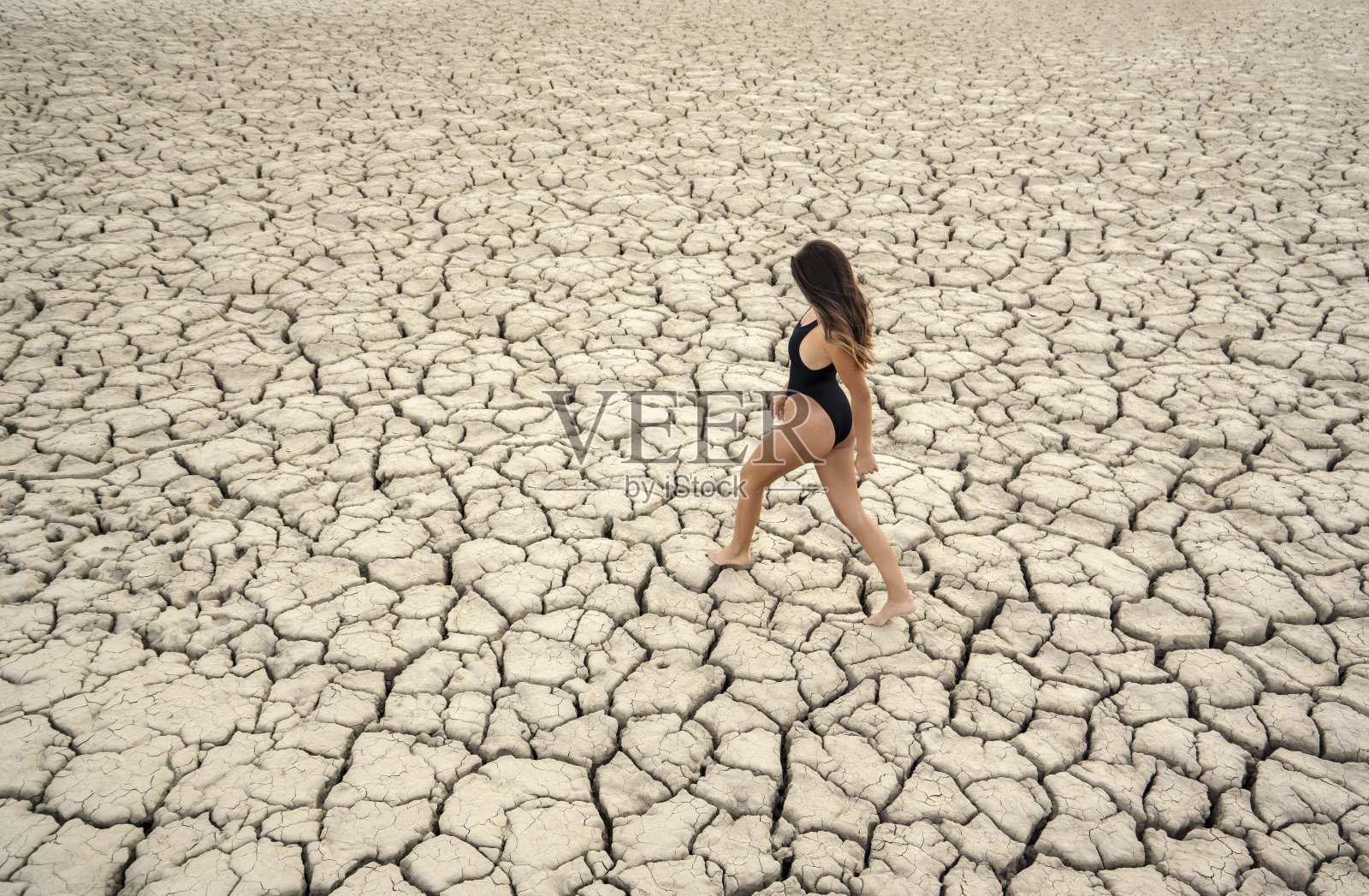 高角度的一个迷人的年轻女子站在开裂的干旱土地，干旱的概念照片摄影图片