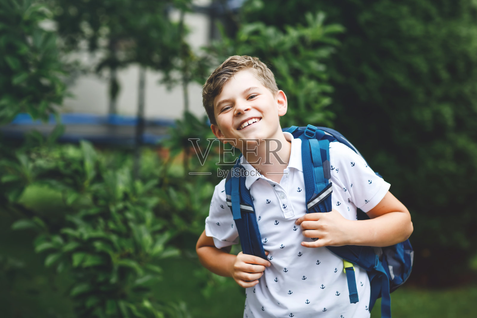 快乐的小男孩背着书包，走着。正在上初中或高中的学生。兴奋的孩子在学校的院子里。回到学校。照片摄影图片