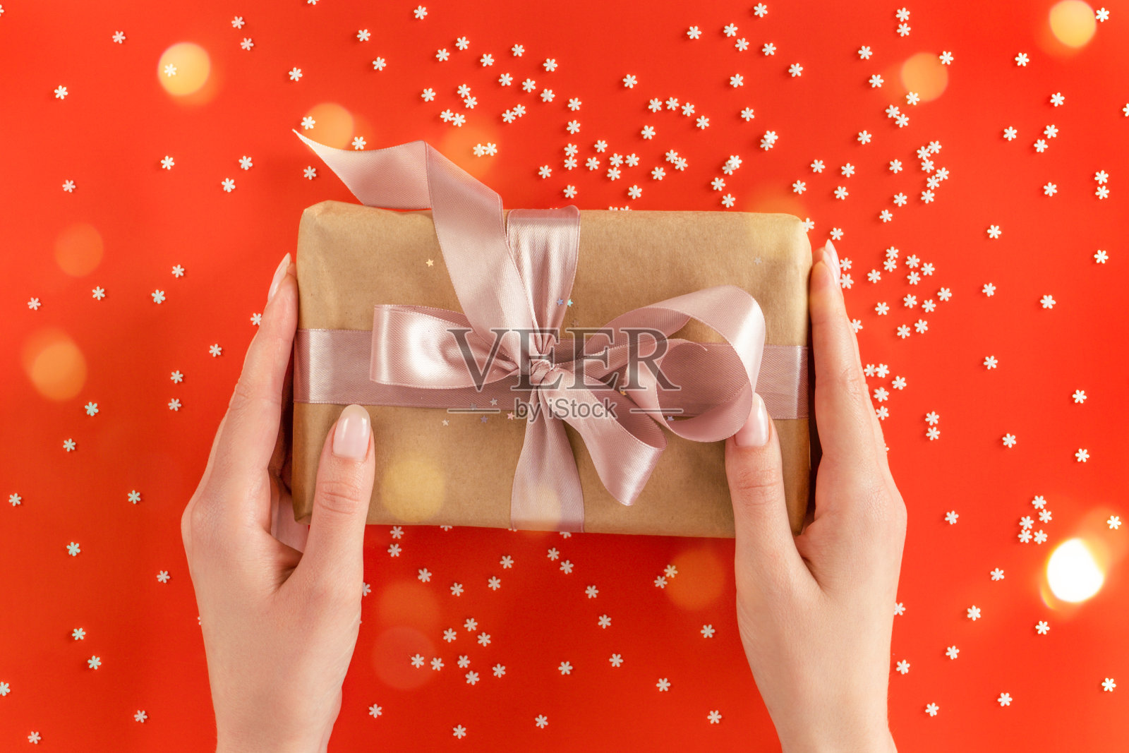 漂亮的女性手捧着用牛皮纸包裹的礼品盒，粉红色的丝带装饰在节日的背景上照片摄影图片