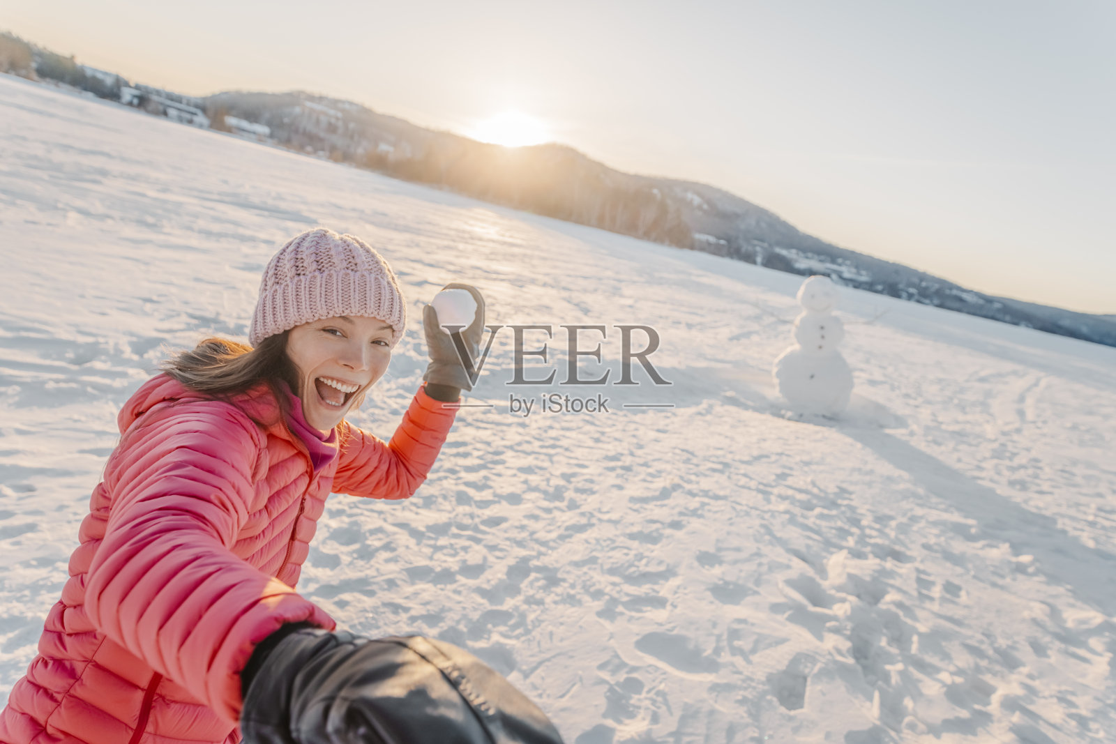 冬天的女孩对着镜头扔雪球，微笑着开心地在雪天玩雪。美丽好玩的多文化的亚洲白人年轻女子户外享受活跃的生活。照片摄影图片