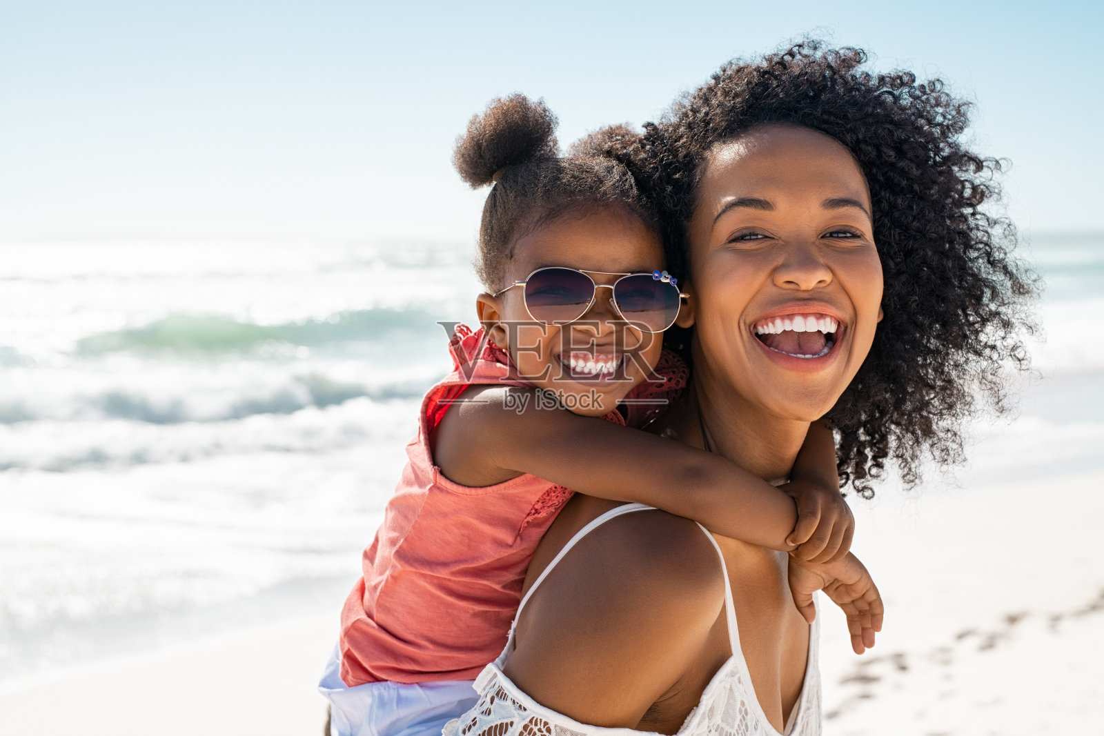 快乐的年轻母亲在沙滩上骑着笑嘻嘻的女儿照片摄影图片