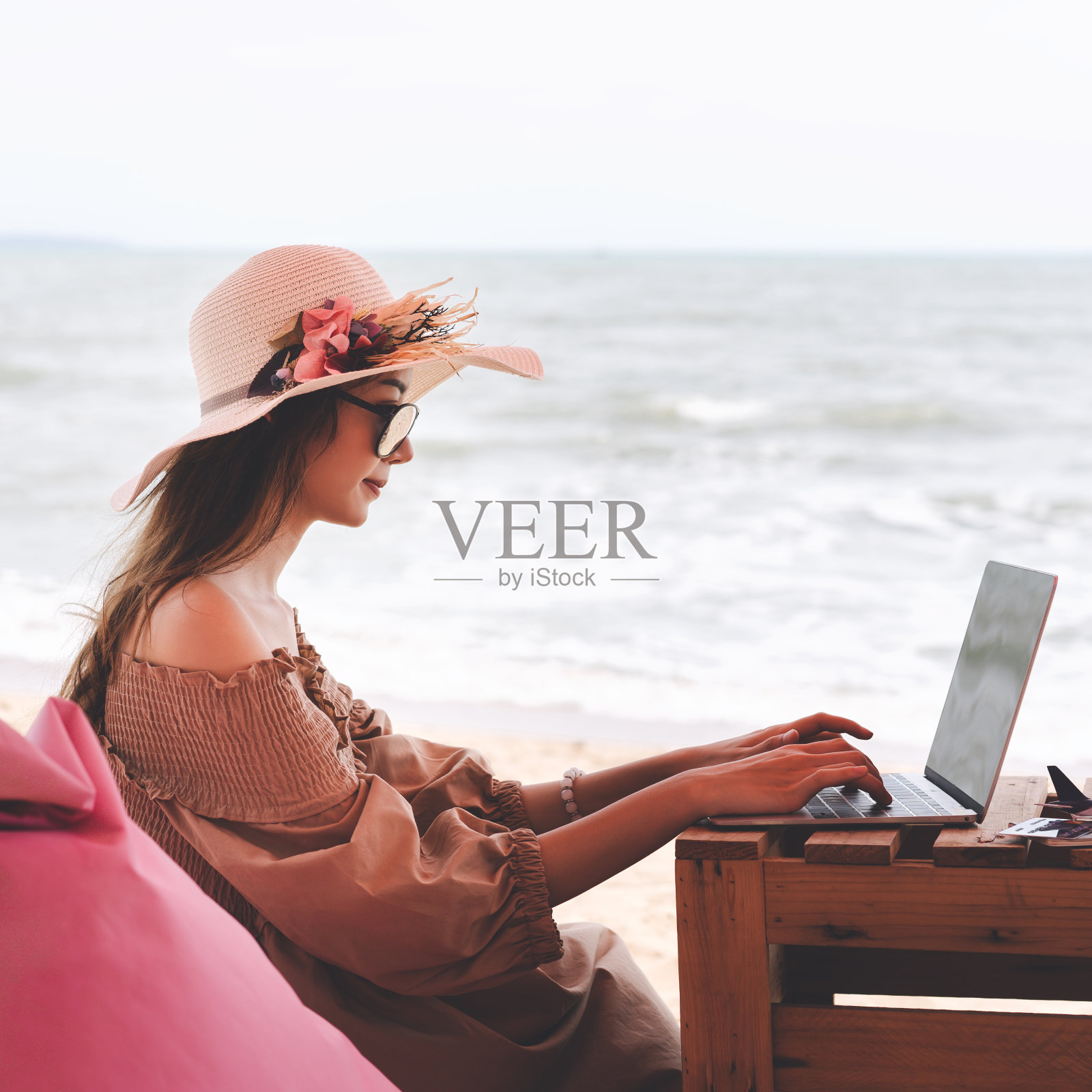 年轻的成年亚洲旅行妇女使用笔记本电脑在海滩工作的一天。照片摄影图片