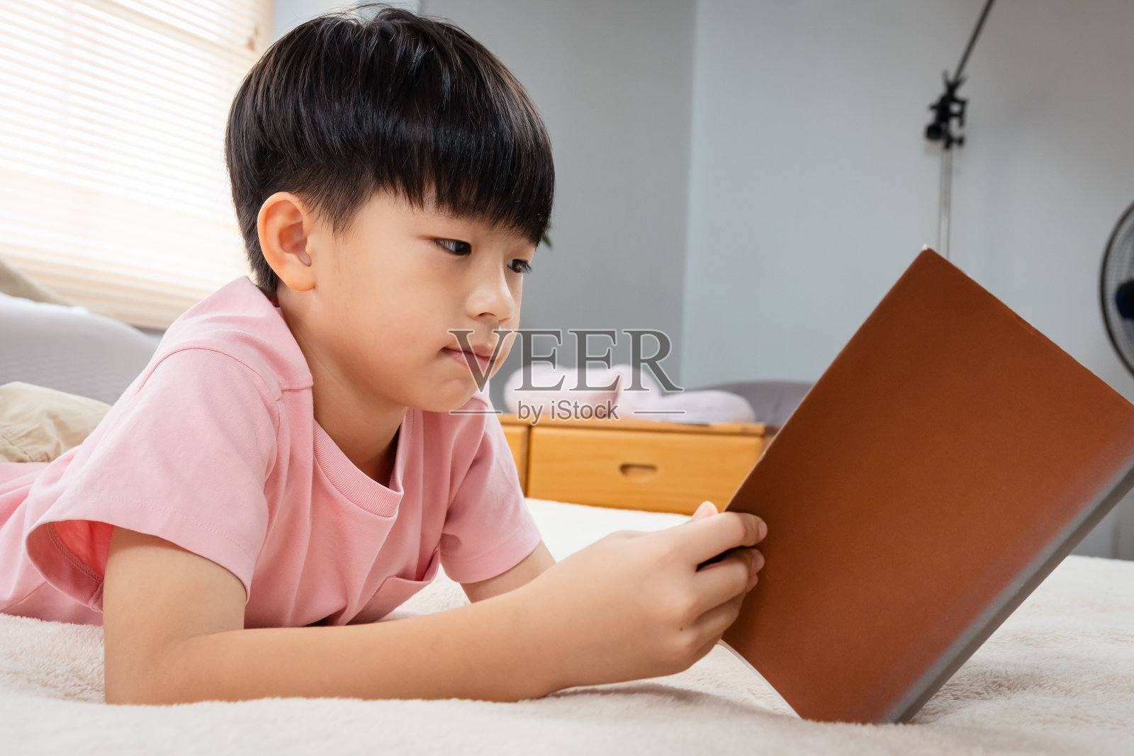 9岁的亚洲男孩坐着看书，他很高兴，每天在卧室的床上复习他学过的东西。照片摄影图片