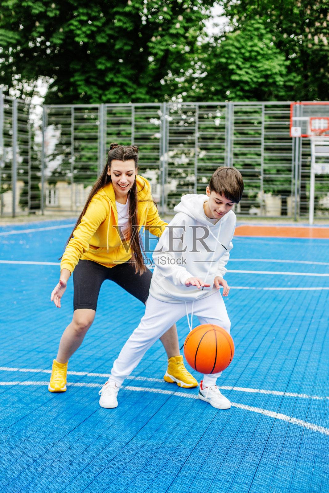女孩和她的弟弟，十几岁，在露天的现代篮球场打篮球照片摄影图片_ID:428998837-Veer图库