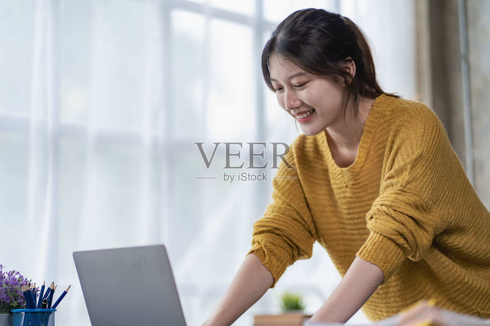 迷人的亚洲女子为她成功地在家里使用笔记本电脑在线工作而高兴。照片摄影图片