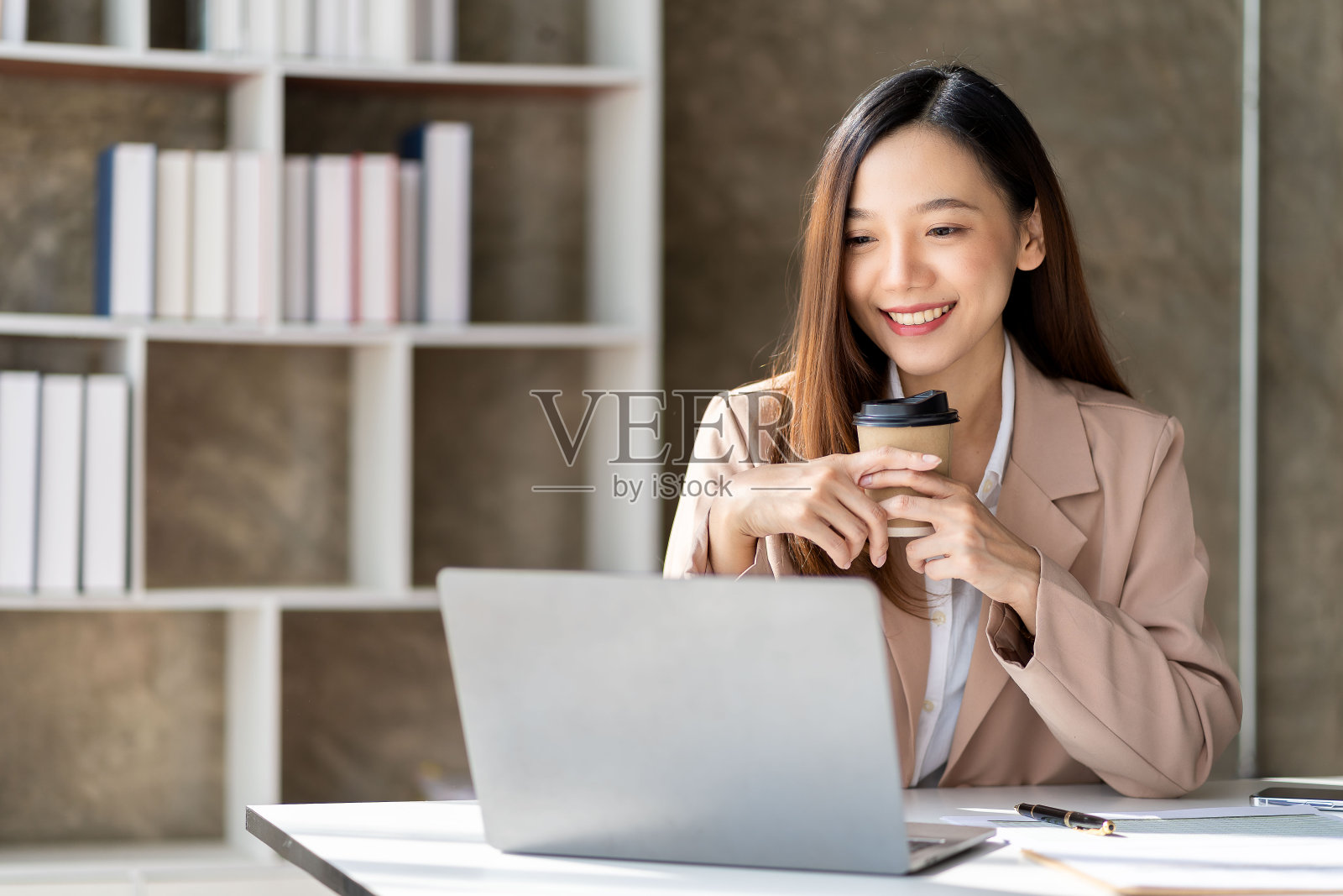 美丽的亚洲女商人微笑着自信和明亮，准备在新的一天工作，喝一杯咖啡。请准备好在笔记本电脑和财务图表面前工作。照片摄影图片