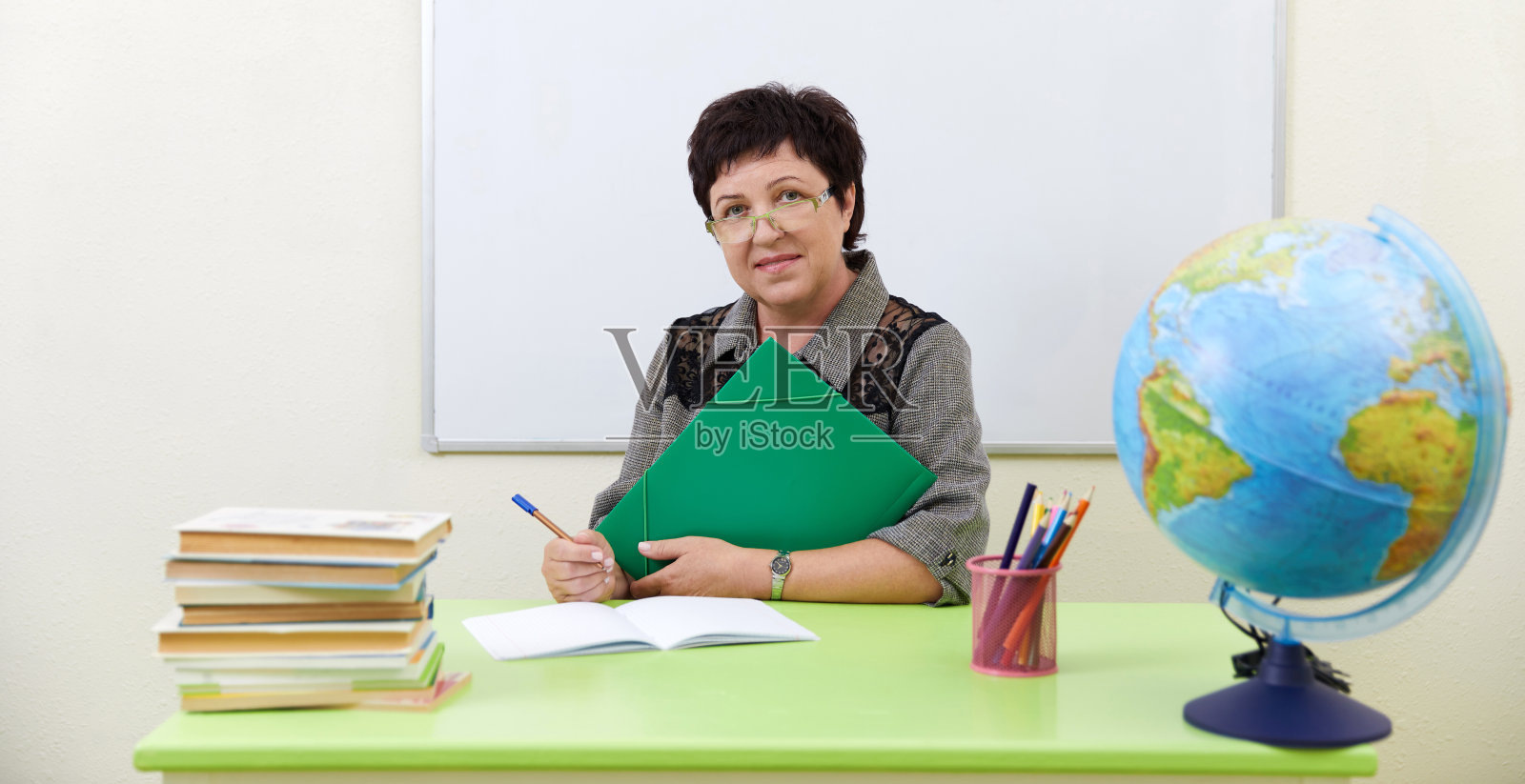 成熟的老师在课前拿着书坐在桌子旁照片摄影图片